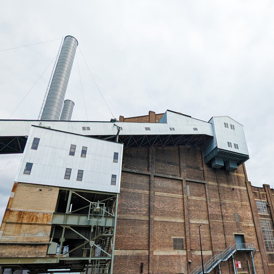 A massive industrial brick building with two round metal smokestacks protruding out the top  towers high against a cloudy sky